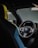 A close-up interior view of a luxury car with a focus on the steering wheel. The steering wheel features multiple buttons and a central logo, surrounded by modern design elements. Parts of the seats with black and blue upholstery are visible, adding to the upscale feel.