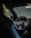 A close-up interior view of a luxury car with a focus on the steering wheel. The steering wheel features multiple buttons and a central logo, surrounded by modern design elements. Parts of the seats with black and blue upholstery are visible, adding to the upscale feel.