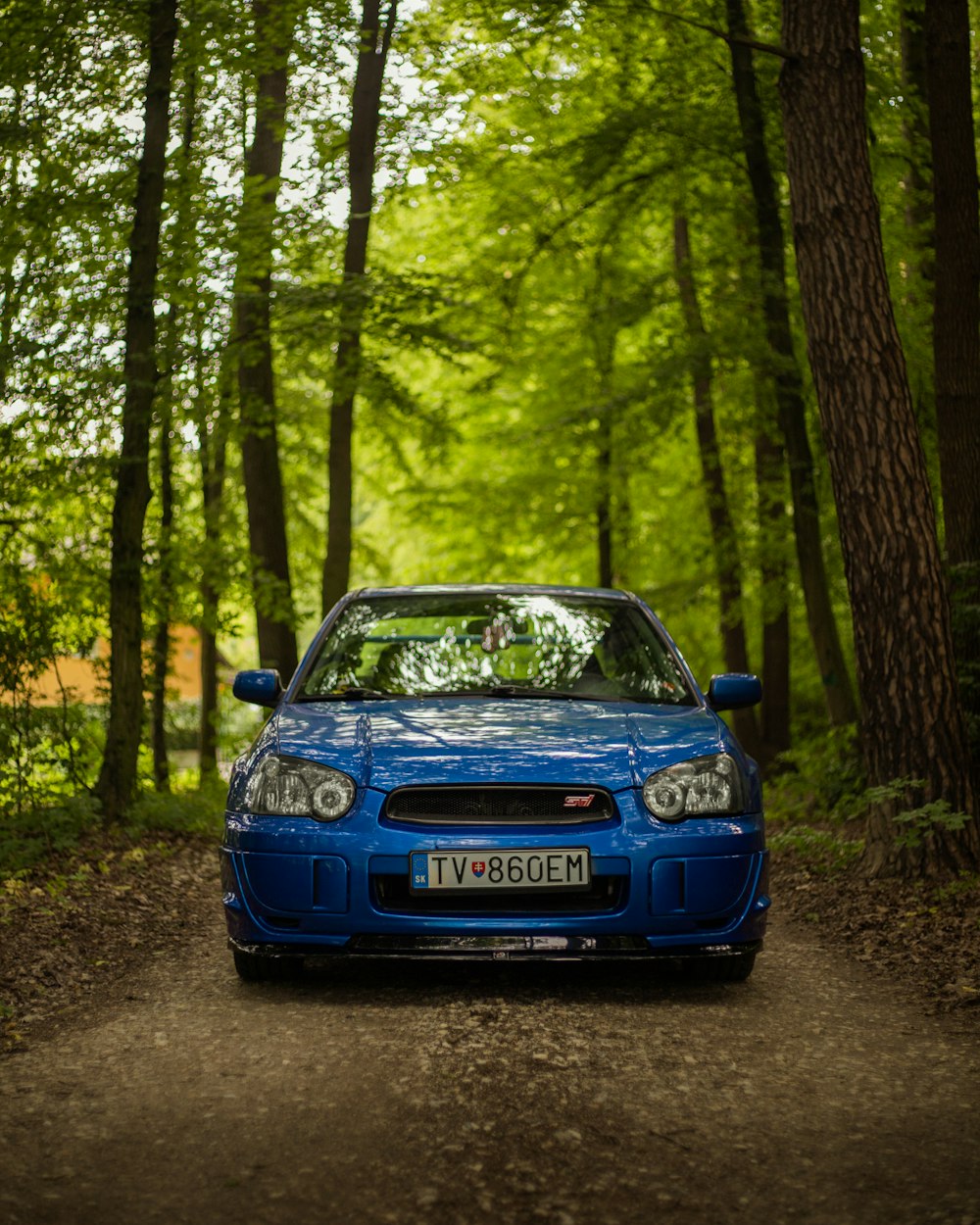 a blue car parked in the middle of a forest