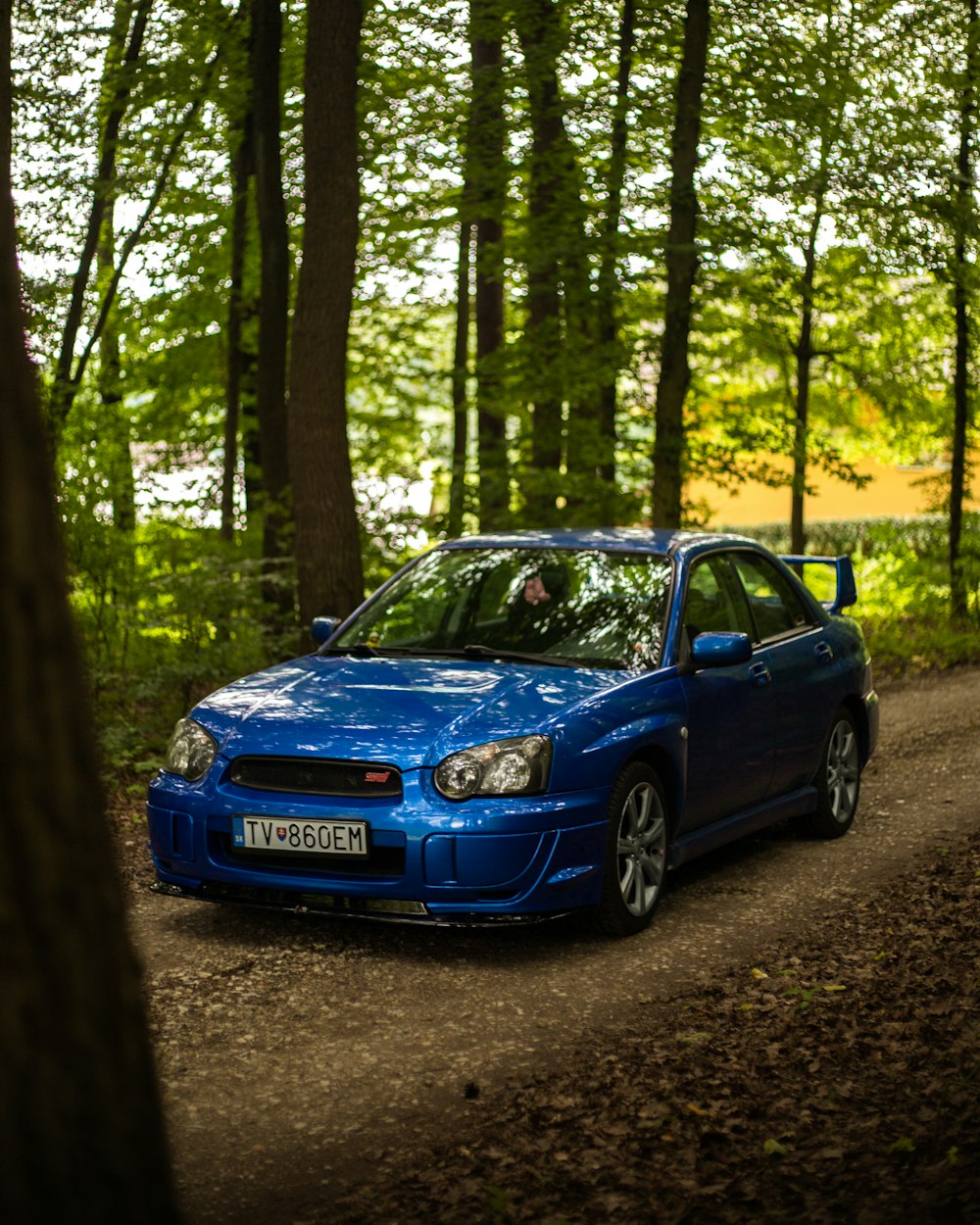 a blue car parked on a dirt road in the woods