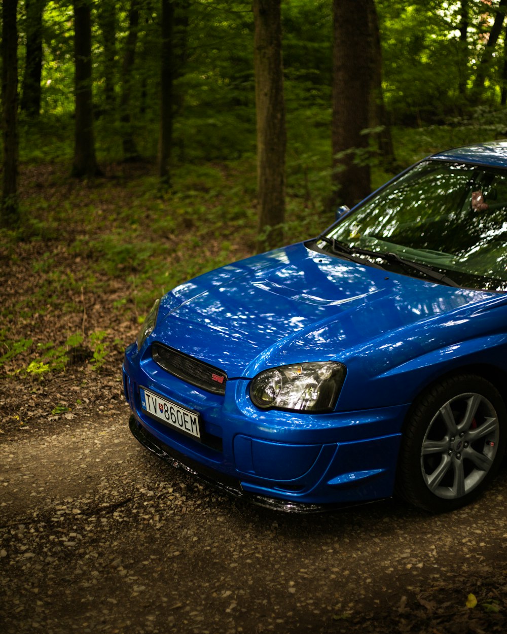 a blue car parked on a dirt road in the woods