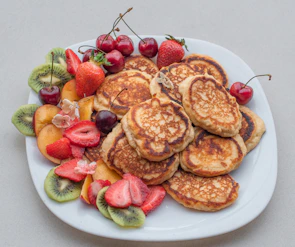 A colorful stack of millet pancakes topped with fresh fruits and nuts, surrounded by smiling children enjoying their snacks.