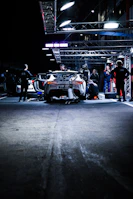 The team mechanics working swiftly on the car in the pit, tools in hand under bright lights.