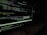 A computer screen displaying code in a dark-themed text editor. The code appears to be written in JavaScript, featuring functions and navigation links. There are file paths and command line interface windows open. A dark environment enhances the glow of the screen.