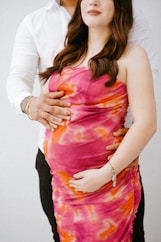 a pregnant woman in a pink dress standing next to a man in a white shirt