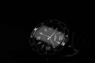 Close-up of a sleek, black-dial wristwatch with luminous hands glowing softly against a dark background.
