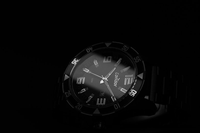 Close-up of a sleek, black-dial wristwatch with luminous hands glowing softly against a dark background.