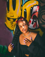 Model wearing layered necklaces and bold earrings against a graffiti wall in a city alley.
