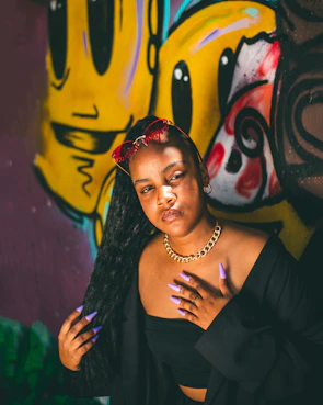 Model wearing layered necklaces and bold earrings against a graffiti wall in a city alley.