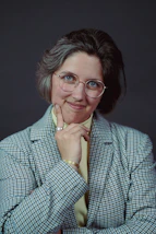 Headshot of a thoughtful speaker wearing glasses and a blazer.