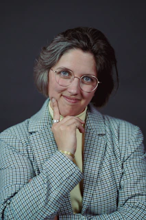 Headshot of a thoughtful speaker wearing glasses and a blazer.