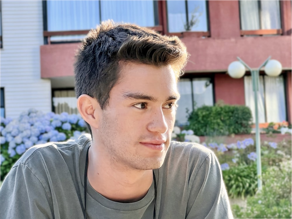 a man with a short haircut sitting in front of a building