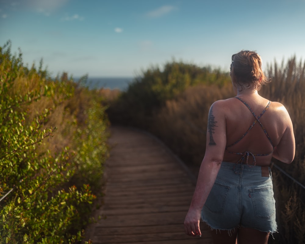 a woman walking down a wooden path next to tall grass