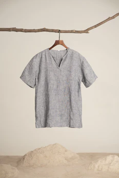 Soft, neutral-toned linen shirt hanging gently on a wooden hanger against a white wall.