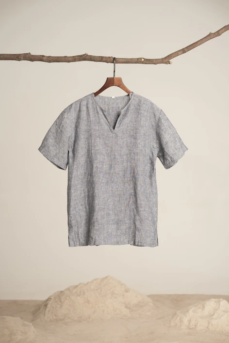 Close-up of a soft linen blouse hanging on a wooden hanger against a white wall.