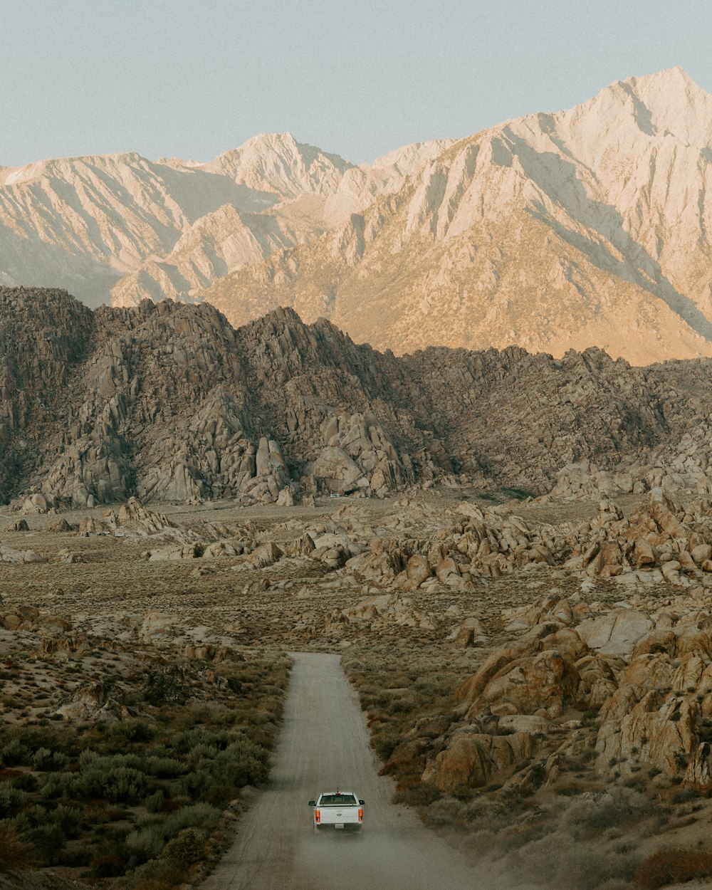 a car driving down a dirt road in front of mountains