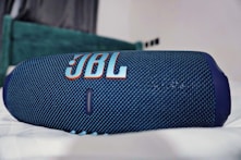 a blue jbl speaker laying on top of a bed