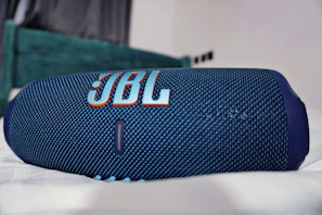 A sleek JBL wireless speaker glowing softly on a wooden table in a cozy living room.