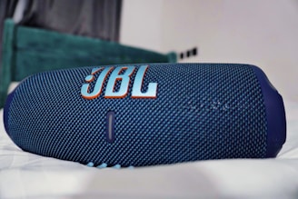 a blue jbl speaker laying on top of a bed