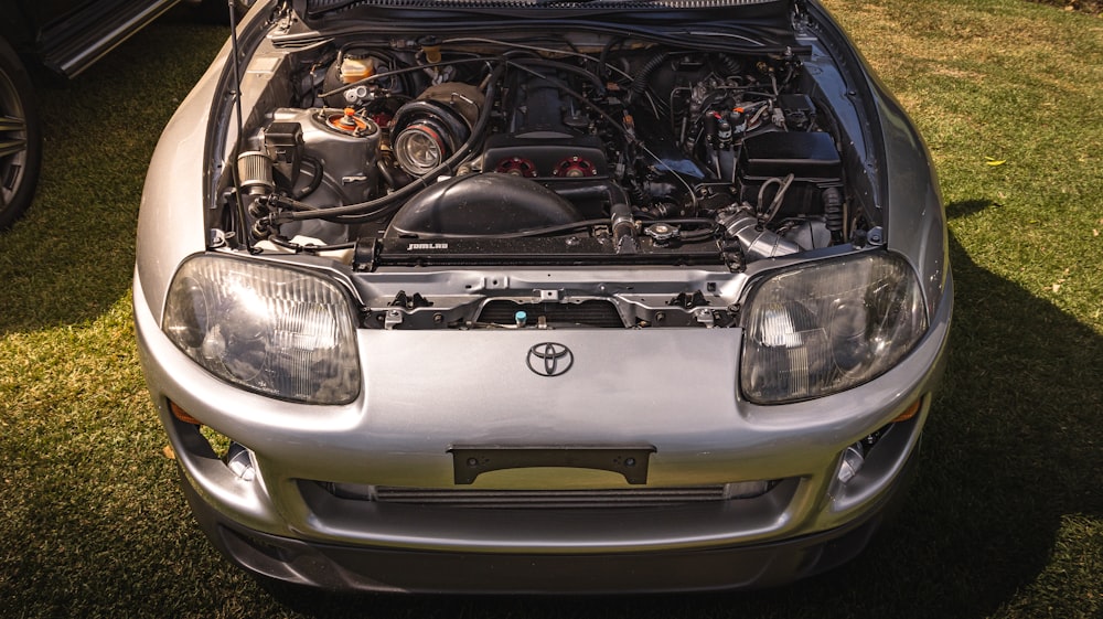 a silver car with its hood open on the grass