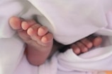 Close-up of tiny baby feet next to a pair of small shoes on a rug.