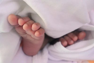 Close-up of delicate baby booties resting beside a tiny knitted hat in gentle cream tones.