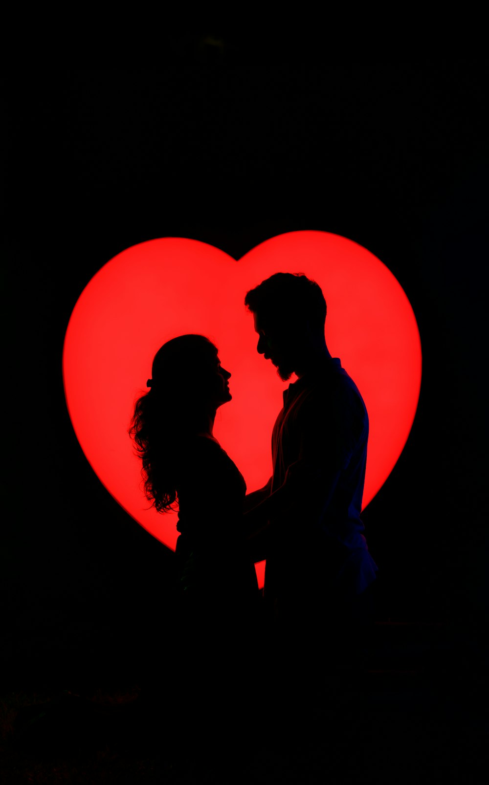 um homem e uma mulher em pé na frente de um coração vermelho