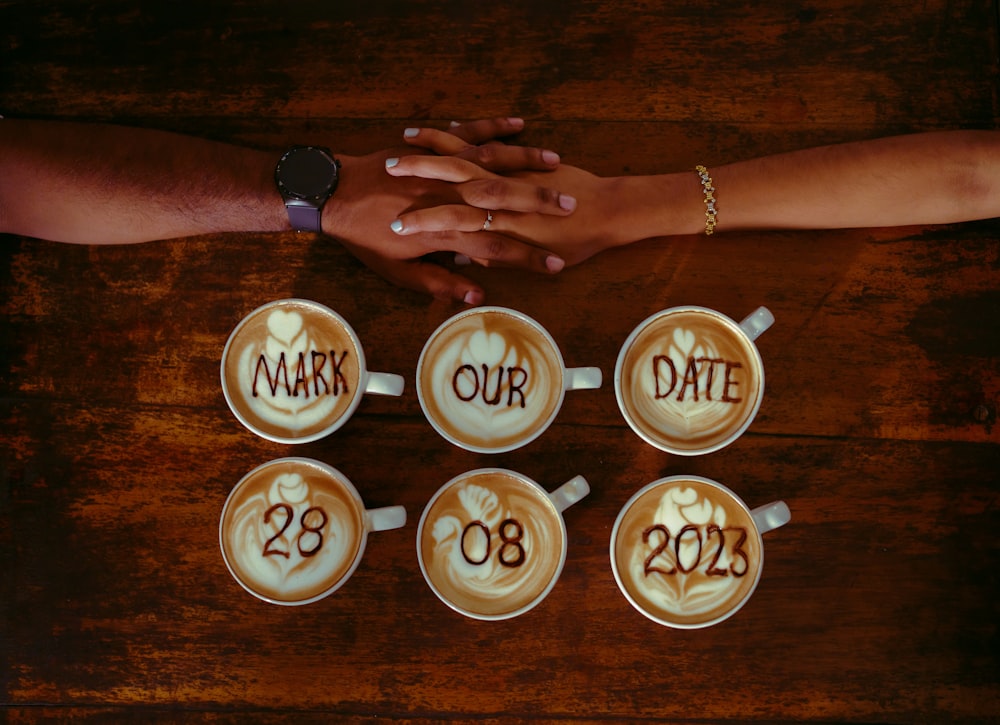 a couple of people holding hands over some cups of coffee