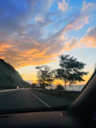 A bold van driving along a coastal highway with vibrant orange accents in the sky.