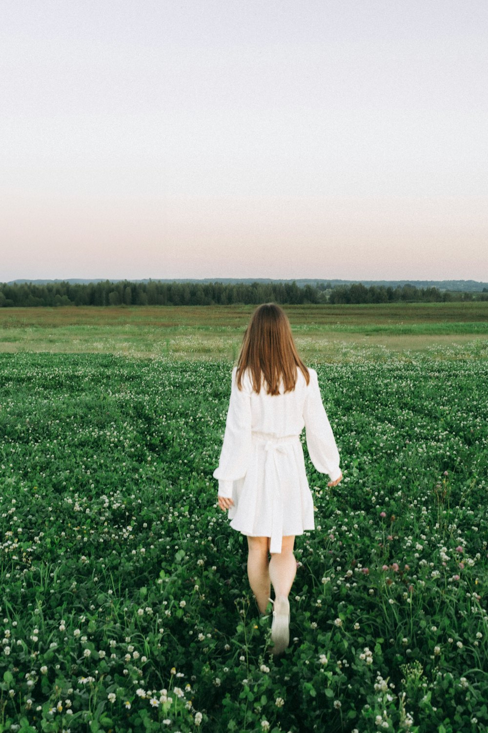 a woman in a white dress walking through a field