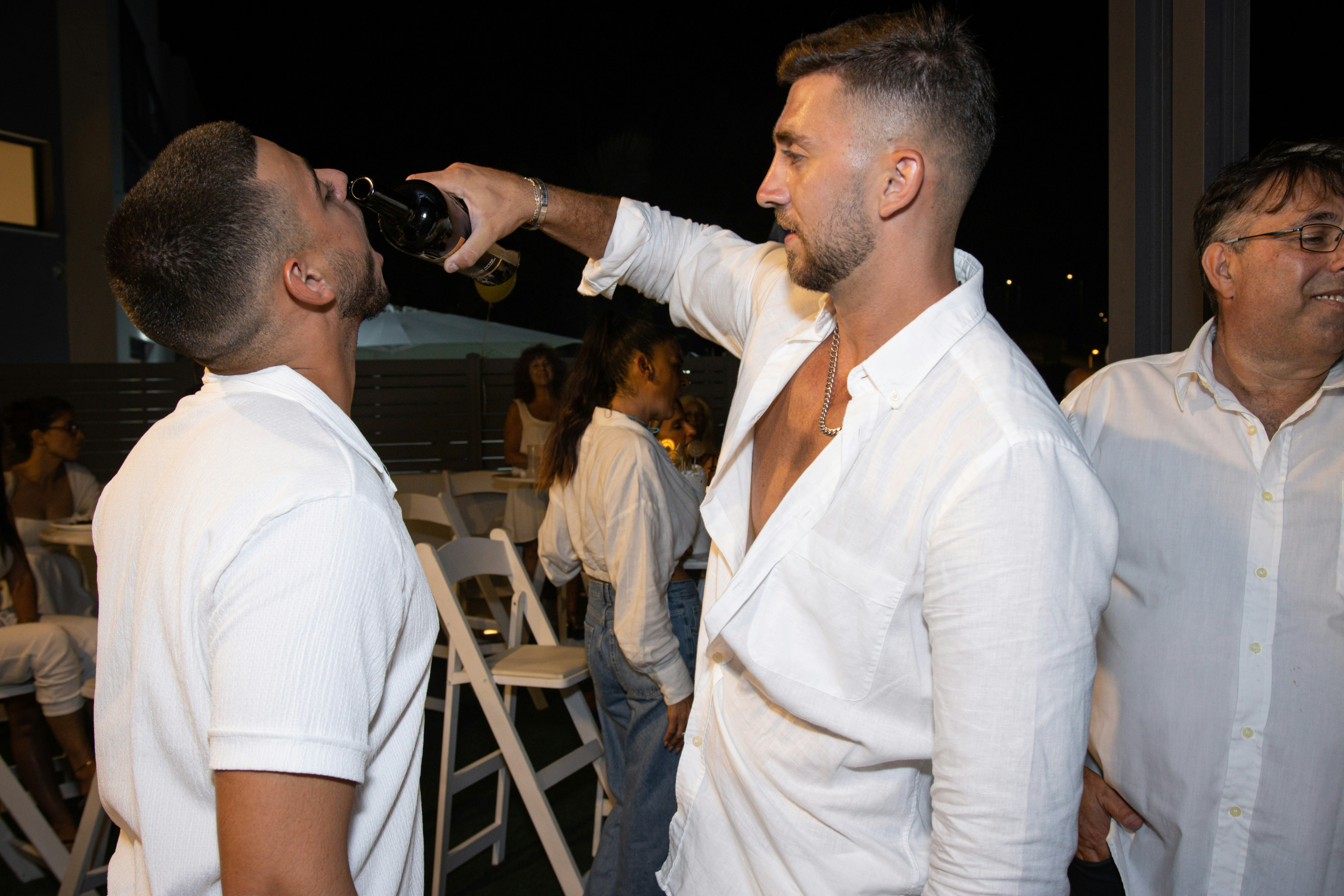 a man drinking from a bottle while standing next to another man