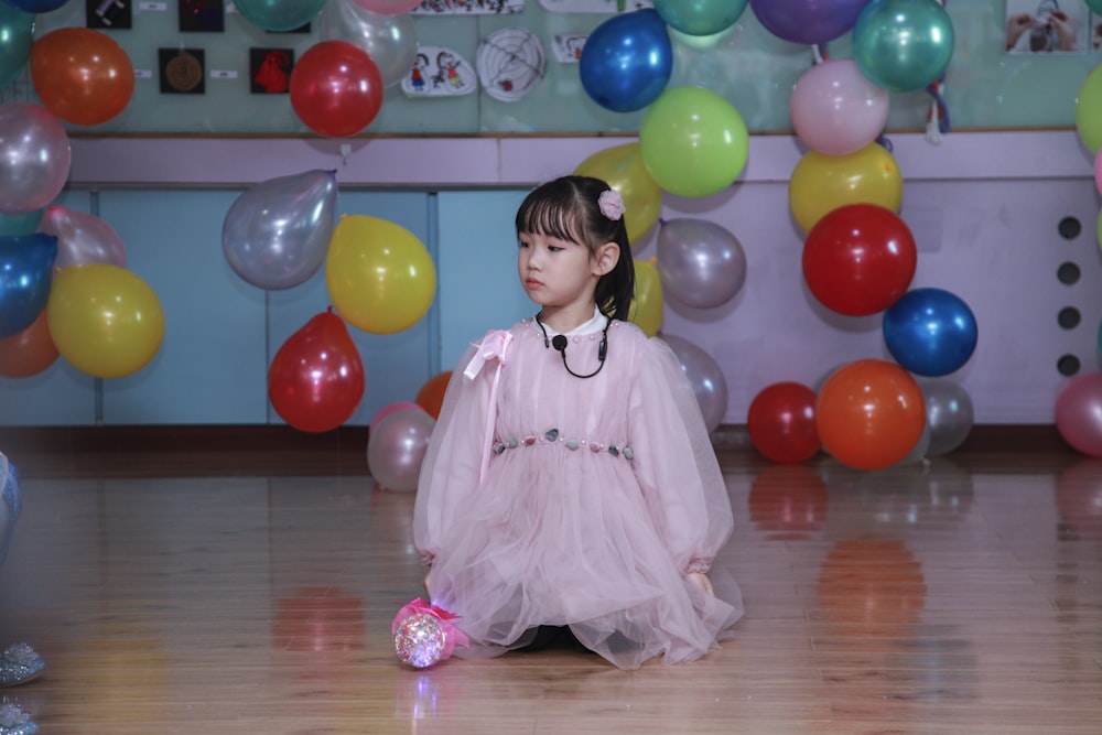 a little girl sitting on the floor in front of balloons