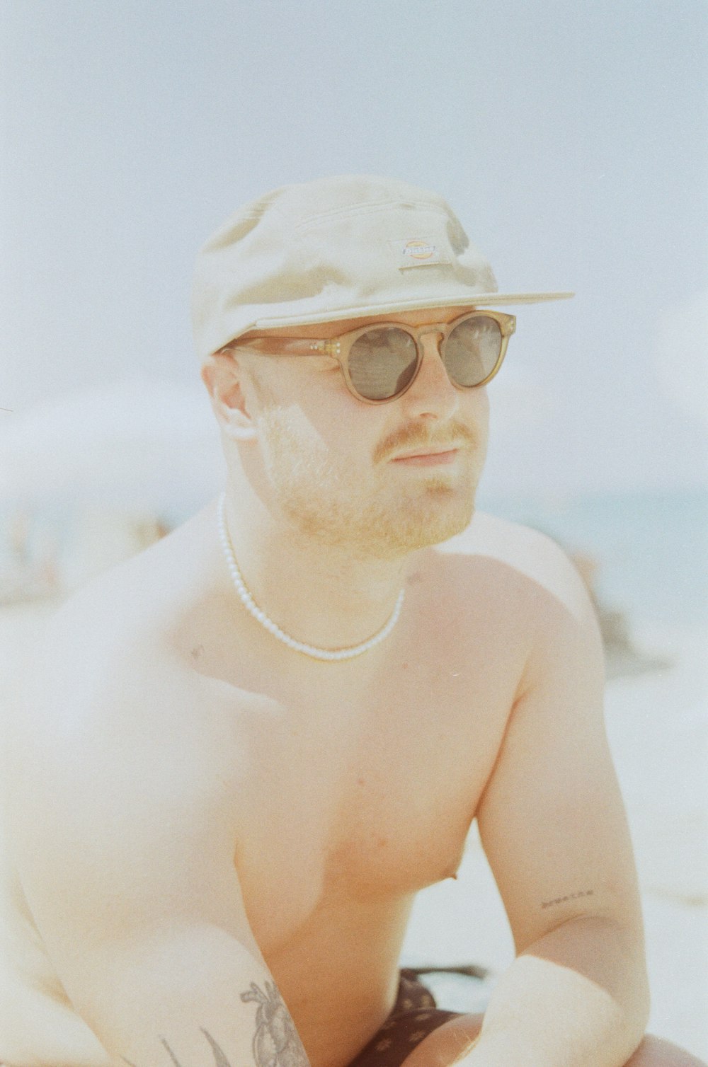a man wearing a hat and sunglasses sitting on the beach