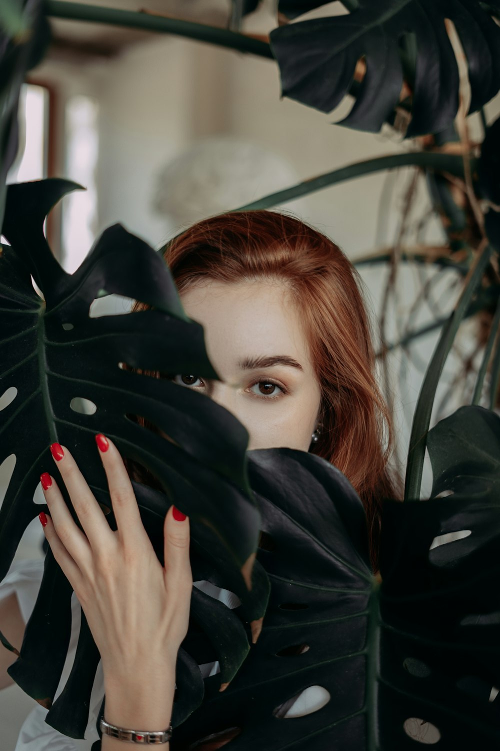 a woman with red nails is hiding behind a large leaf