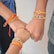 Three hands close together, each wearing a colorful, beaded bracelet. The bracelets feature intricate designs with red, orange, gold, and pearl-like beads. The hands are in a gesture that suggests unity or solidarity.