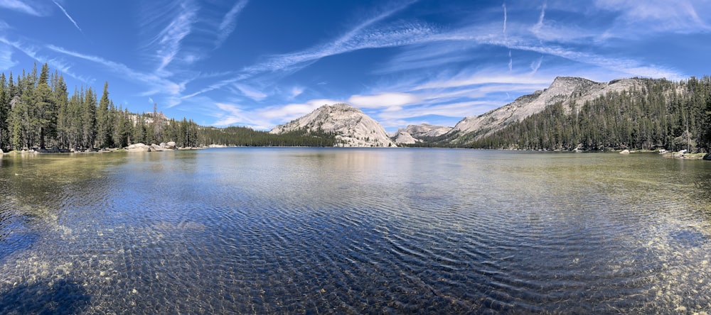 a lake surrounded by trees and mountains under a blue sky