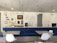 A modern interior space with a blue upholstered bench, white chairs, and tables. The wall features motivational quotes and words arranged in creative patterns. Decorative elements include hanging light fixtures and potted orchids. The overall ambiance is clean and inspiring.