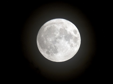 A large, bright full moon with detailed surface features such as craters and lunar maria, set against a dark night sky.