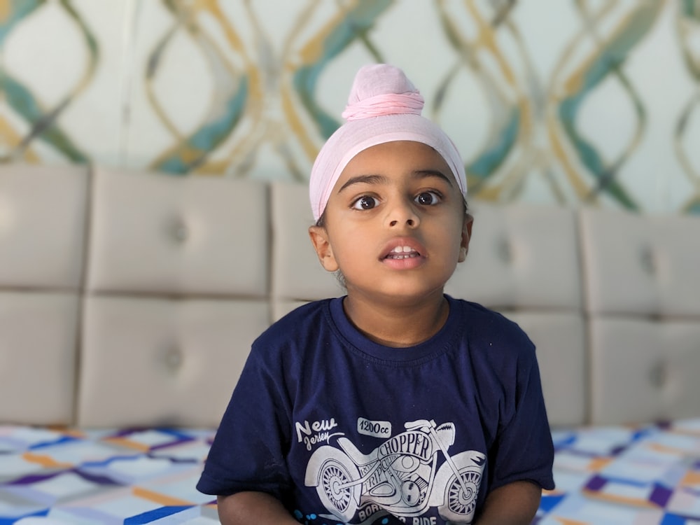 a young boy wearing a pink hat sitting on a bed