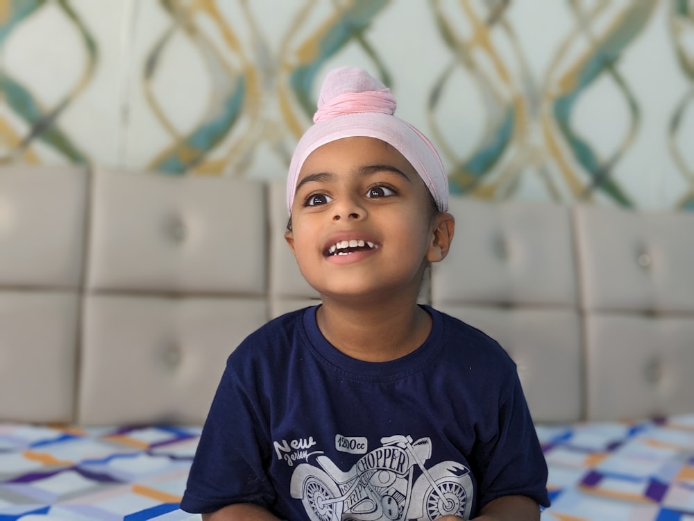 a young boy wearing a pink turban sitting on a bed