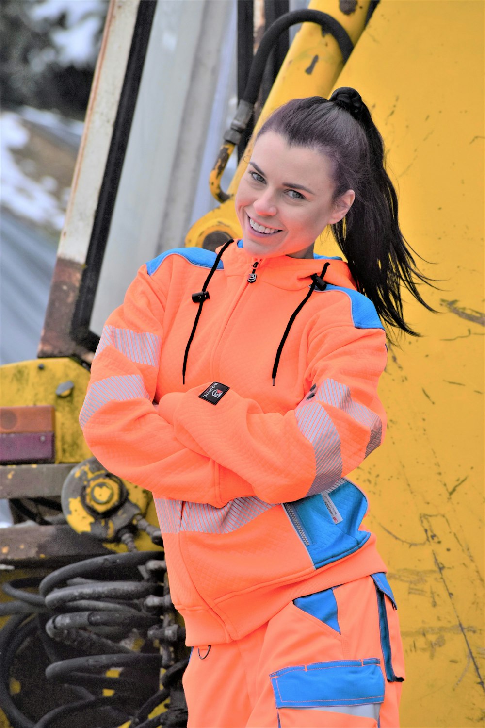 a woman in an orange jacket standing next to a forklift