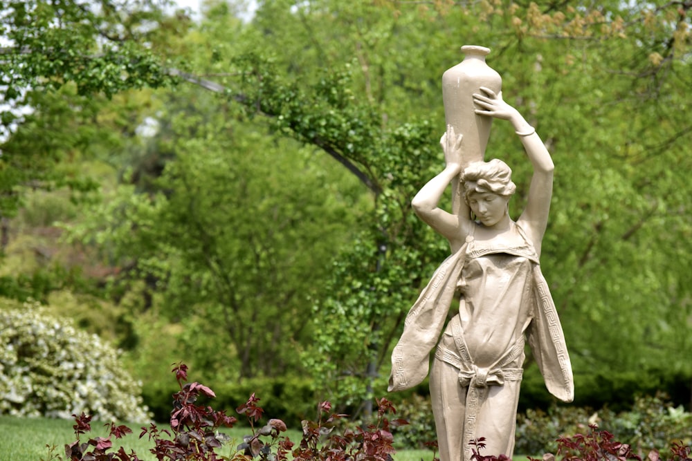 a statue of a woman holding a vase in a garden
