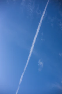 Crystal-clear blue sky framing a jet trail gracefully arching across the horizon.