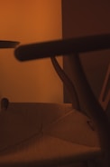 A close-up shot of a wooden chair with woven seat details, set against a warm, softly lit background. The image emphasizes the curved design of the chair's arms and legs, creating a cozy and inviting atmosphere.