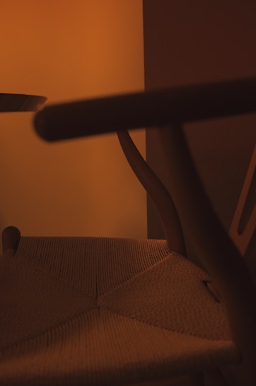 A close-up shot of a wooden chair with woven seat details, set against a warm, softly lit background. The image emphasizes the curved design of the chair's arms and legs, creating a cozy and inviting atmosphere.