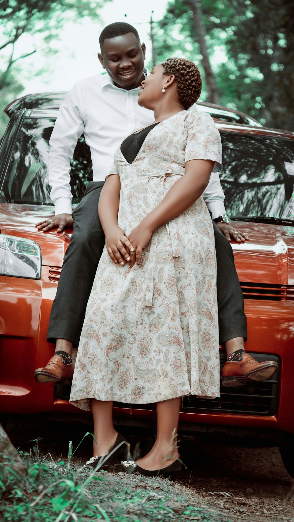 a man and woman sitting on the hood of a car