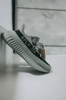 Minimalist Yeezy sneakers resting on a dark grey surface with a faint neon outline.