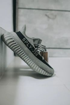 Minimalist Yeezy sneakers resting on a dark grey surface with a faint neon outline.