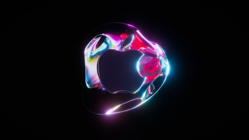 A stylized logo resembling an apple with a smooth, reflective, and metallic finish. The surface displays vibrant and swirling neon colors including pink, blue, and purple, set against a dark background.