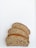 Three slices of brown bread are arranged on a white surface. The bread has a dense and slightly grainy texture with visible seeds and a golden brown crust.